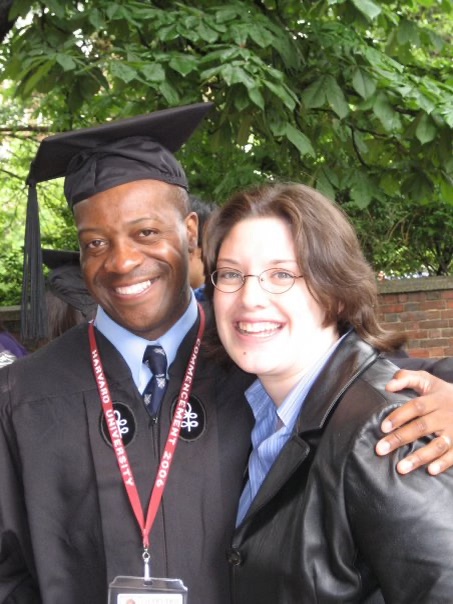 Siza Mtimbiri smiles next to his wife while wearing a cap and gown at Commencement.