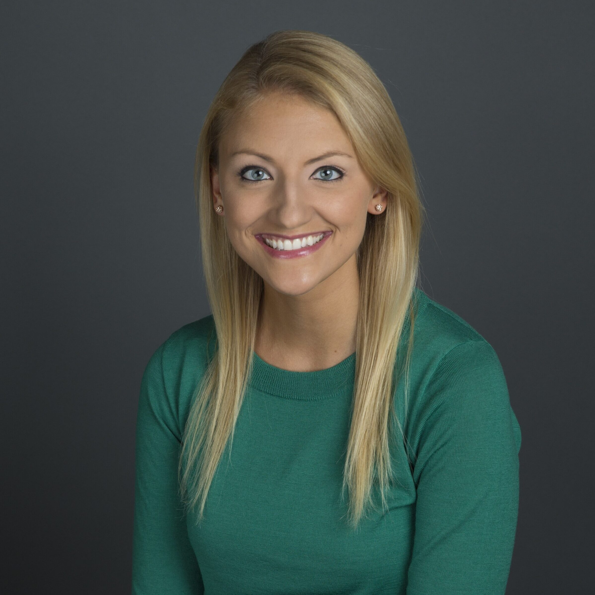 Blonde woman with light skin in a green shirt smiling/