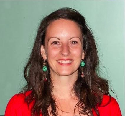 Woman with light skin and dark hair and green earrings smiling