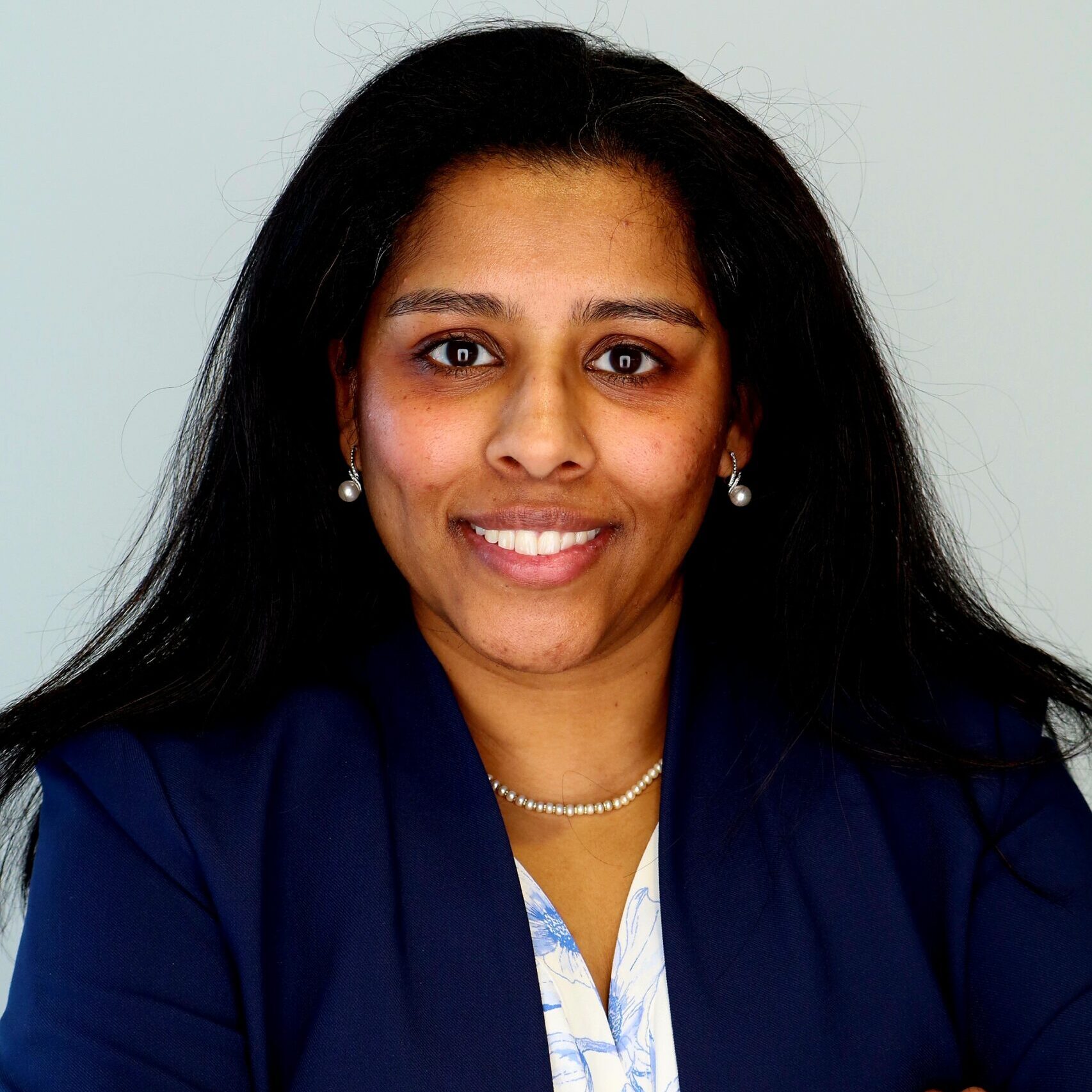 Headshot of woman with dark skin and hair with her hands crossed